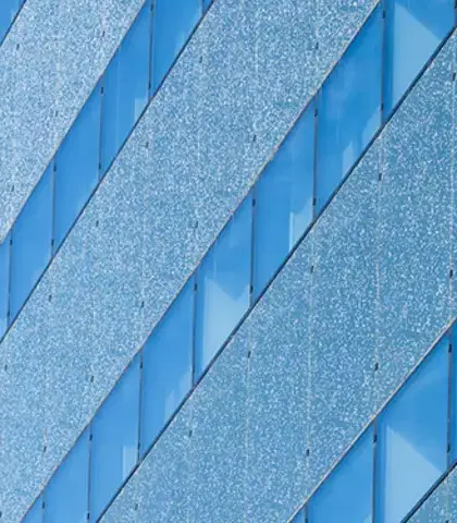 Modern gebouw met een unieke glazen gevel, versierd met reflecterende patronen, tegen een blauwe lucht