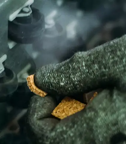 close-up van een met handschoenen beschermde hand die werkt aan een machine met glazen componenten in een industriële omgeving